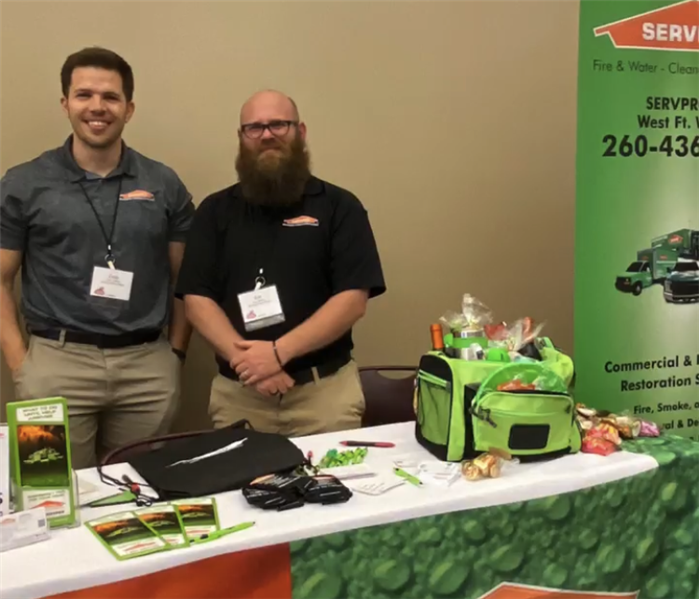 Two men standing behind a colorful SERVPRO table display.